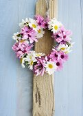 Wreath of pink and white daisies on wooden board
