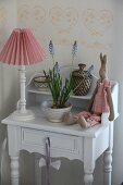 Table lamp with red and white lampshade, plush rabbit and grape hyacinths on small, shabby-chic cabinet