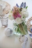 Spring bouquet with white ranunculus and hyacinths in screw-top jar and ornamental eggs decorated with lace ribbons and feathers on table set for Easter
