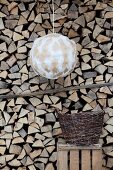 Pendant lamp with hand-crafted spherical lampshade in front of stacked firewood