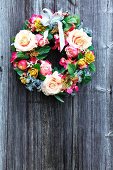 Decorative wreath of various flowers with ribbon on wooden wall