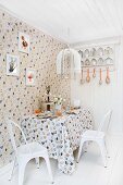 Dining area set for Easter in kitchen decorated with hen motif on wallpaper and tablecloth and white, vintage chairs