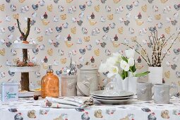 Serviette, Tischdecke und Tapete mit farbigen Hühnermotiven und graues Geschirr mit Hühnerrelief auf Ostertisch