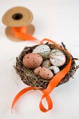 Gesprenkelte Eier im Osternest aus Weidengeflecht mit orangefarbenem Geschenkband