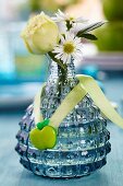 Rose and chamomile flowers in small blue vase decorated with apple-shaped button
