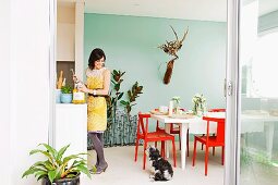 Red chairs at white table in dining room with pastel turquoise wall; counter, woman and dog to one side