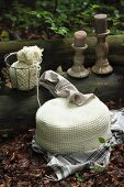 White, crocheted pouffe and candlesticks on tree trunk in woodland