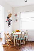 Tripp Trapp Kinderstuhl und rustikale Stühle mit blaugrüner Sitzfläche am runden Tisch vor Fenster, an Wand Hirschtrophäe aus geschnitztem Holz und Fotosammlung