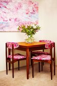 Wooden chair with patterned fabric seats and backrests around bouquet on table below large picture on wall