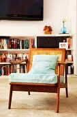 Biedermeier Sessel mit Rückenlehne aus Geflecht und pastellfarbene Rücken- und Sitzpolster auf Teppichboden, im Hintergrund halbhohes, weisses Bücherregal