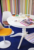 Mixture of patterns - white, round table, shell chairs with colourful seat cushions on blue patterned rug and striped wallpaper