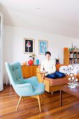 Klassiker Sessel mit hellblauem Bezug und Frau auf Sofa in Wohnzimmer mit Dielenboden
