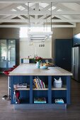 Large island counter with integrated, blue-painted shelves below ceiling lamp suspended from exposed roof structure