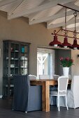 Various chairs at rustic table below vintage pendant lamps made from red-painted metal suspended from roof beams