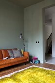 Light green woollen rug, pastel green walls, comfortable, cognac leather sofa with scatter cushions and standard lamp in corner