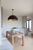 Open-plan kitchen with white furniture and set wooden table below black pendant lamp