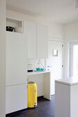 Simple, white fitted kitchen with bright yellow retro bin