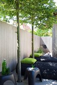 Black floor-cushion loungers with green pillows and plastic stools on terrace with wooden fence