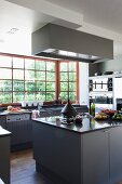 Essensvorbereitung auf Mittelblock mit grauen Unterschränken gegenüber Küchenzeile an Sprossenfenster mit Gartenblick