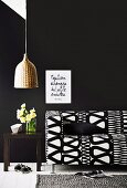 Sofa with black and white geometric cover against black wall and pendant lamp with wicker lampshade