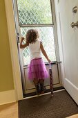 Mädchen mit violettem Tüllrock schaut durch die verglaste Tür ins Freie