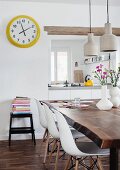 Dining area in mixture of styles - classic chairs at rustic walnut table and yellow-framed station clock next to hatch