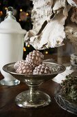 Fir cone baubles in silver footed dish and white glass vessel with lid on table