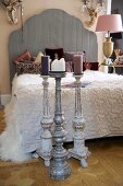 Floor-standing candlestick in front of French bed with wooden headboard next to bedside lamp with pink lampshade