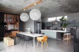 Open-plan, designer kitchen-dining area with elegant, purist, fitted wooden partition shelves; two spherical pendant lamps hanging from concrete ceiling