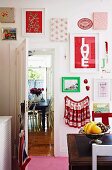 Gerahmte, farbige Stoffmuster und Bilder an Küchenwand, Obstschale auf antiquarischem Holztisch, im Hintergrund offene Tür und Blick auf Essplatz