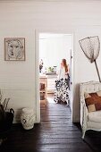 Blick vom Vorraum mit Fischernetz und Vintage Sessel an weisser Holzwand, in Nebenraum mit durchgehendem, dunkelbraunem Dielenboden, Frau mit zwei Dalmatiner in Küche