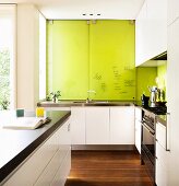 Modern white designer kitchen with writing on lime green sliding cupboard doors above sink