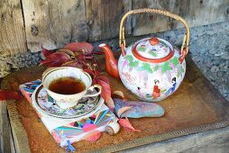 Vintage teacup, saucer and Chinese china teapot on rusty tray decorated with Virginia creeper leaves