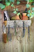 Gardening utensils on wall-mounted shelf made from a quarter-circle log, round hooks and metal brackets