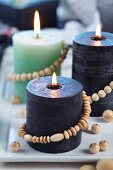 Verschiedenfarbige Kerzen mit Holzperlenkette dekoriert