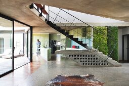 Purist house with exposed concrete ceiling and glass wall with view of courtyard; wine rack in concrete plinth of free-standing staircase