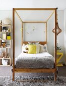 Four-poster bed with scatter cushions and mobile hanging from wooden frame next to modern wooden shelves of soft toys in teenager's bedroom with grey carpet and rug