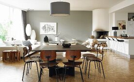 Classic wooden chairs at large dining table below pendant lamp; lounge area next to window in background opposite open-plan kitchen