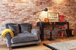 Couch with grey upholstery next to black metal table and vintage swivel chairs against illuminated brick wall