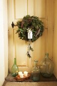 Festive wreath on vintage interior door and collection of glass bottles on floor in door niche