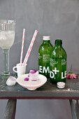 Cosmos petals frozen into ice cubes, lemonade in green bottles and stripes paper straws on rustic stool