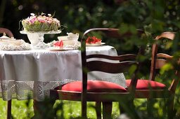 Romantically set coffee table in garden with white tablecloth and nostalgic, upholstered wooden chairs
