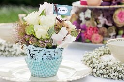 Romantic arrangement of flowers and place card on garden table set for festive afternoon tea party
