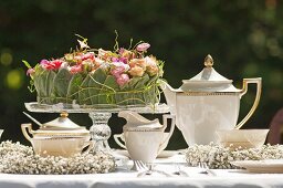 Elegant, romantic coffee table in garden set with flower arrangement on glass cake stand and delicate wreaths of gypsophila