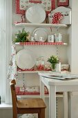 Sales room with white, country-style china displayed on shelves decorated with red and white gingham fabric
