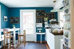 Nostalgic sales room with bistro stools, white counter table and blackboards on blue walls; country-house ambiance