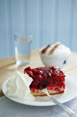 Slice of cherry cake and cream on white plate and blue and white checked napkin