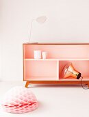 Pendant lamp with copper shade, pink table lamp, pink sideboard with champagne-coloured interior and honeycomb paper ball