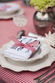 China plate with raised pattern on red and white striped tablecloth and napkin tied with ribbon