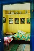 Blick in Schlafraum auf Einzelbetten, vor gelb lackierten Wänden mit gerahmten Bildern und religiösen Motiven